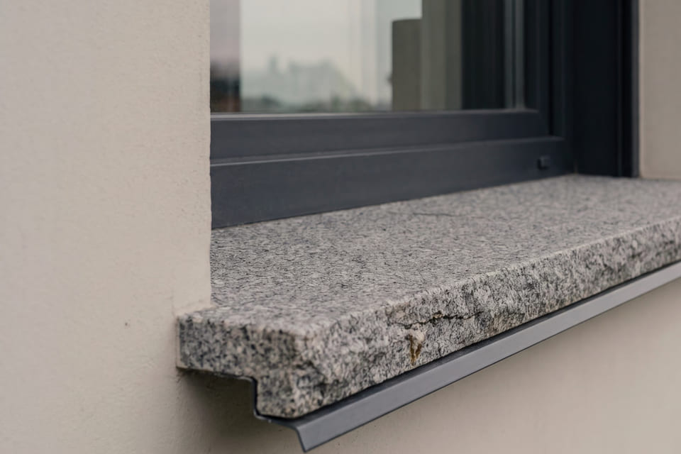 Zewnętrzny parapet z szarego granitu z okapnikiem pod ciemną ramą okna