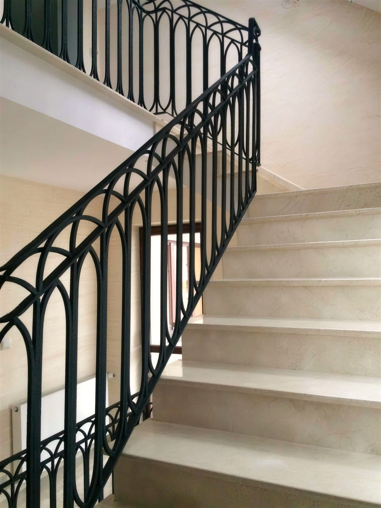 Jasne kamienne schody za kutą balustradą o łukowym rysunku