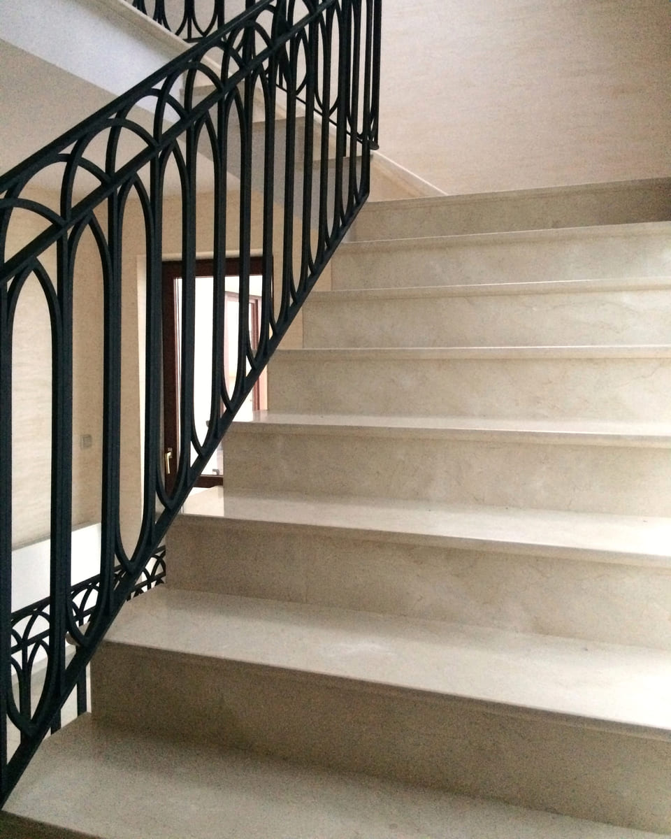Bieg jasnych kamiennych stopni widziany zza kutej balustrady
